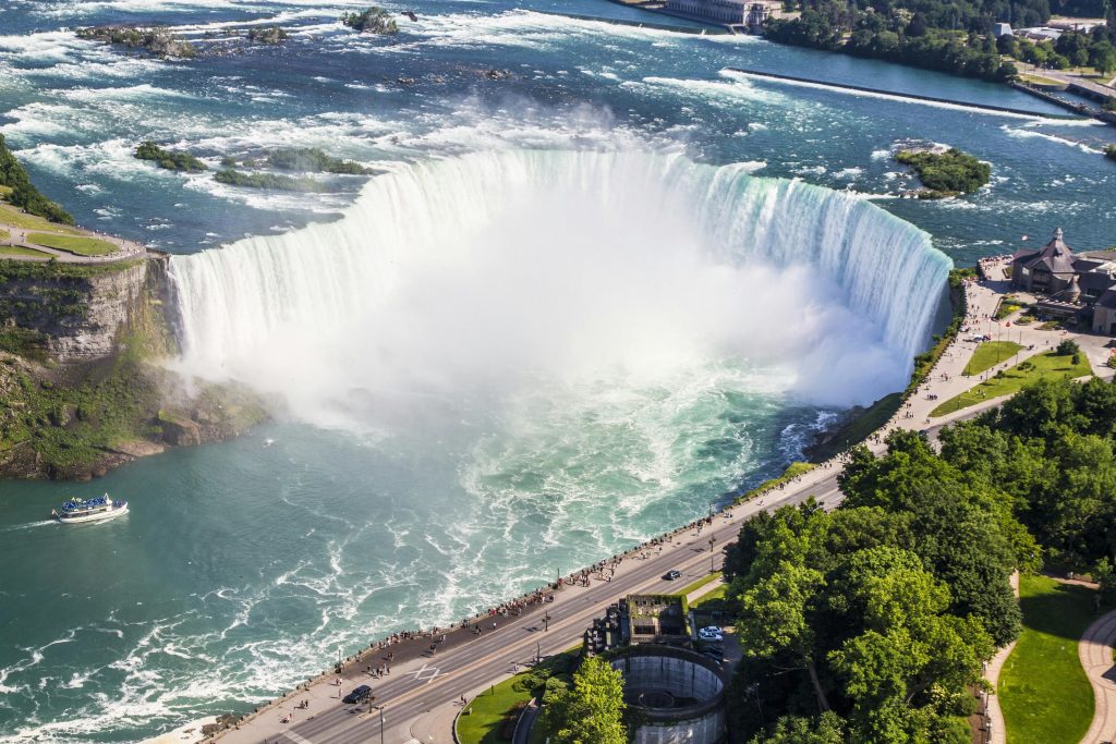 Stunning aerial shot of Niagara Falls with a boat tour and lush greenery on a sunny summer day.