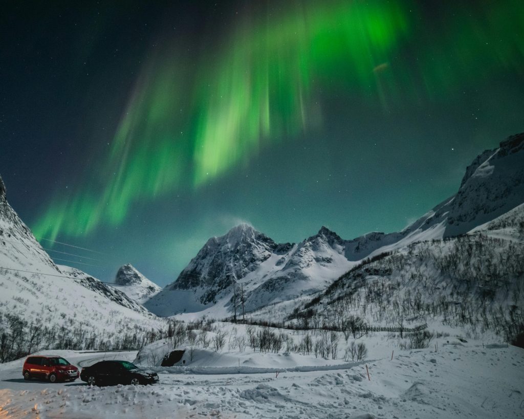 Capture of the breathtaking aurora borealis over snow-covered mountains in Tromsø, Norway at night.